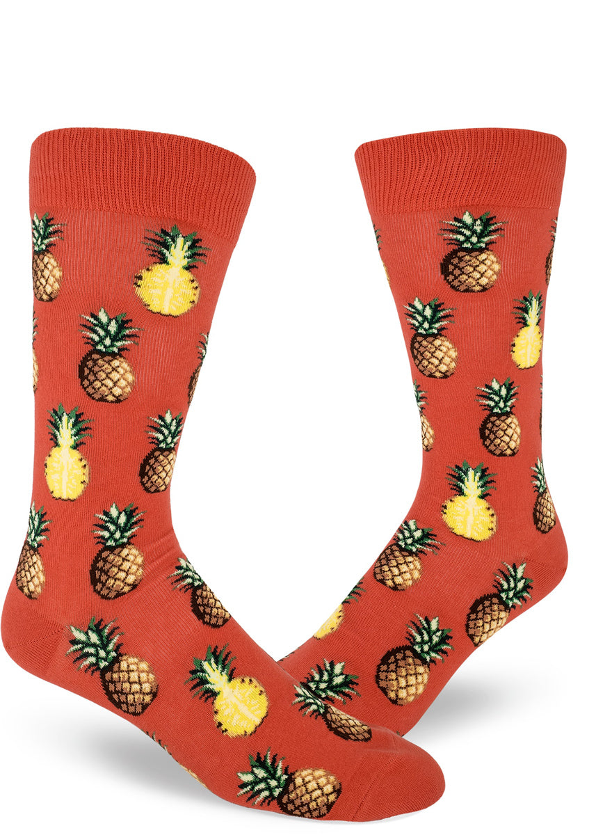 Tropical pineapple socks for men with pineapples sliced in half or whole on a coral red background