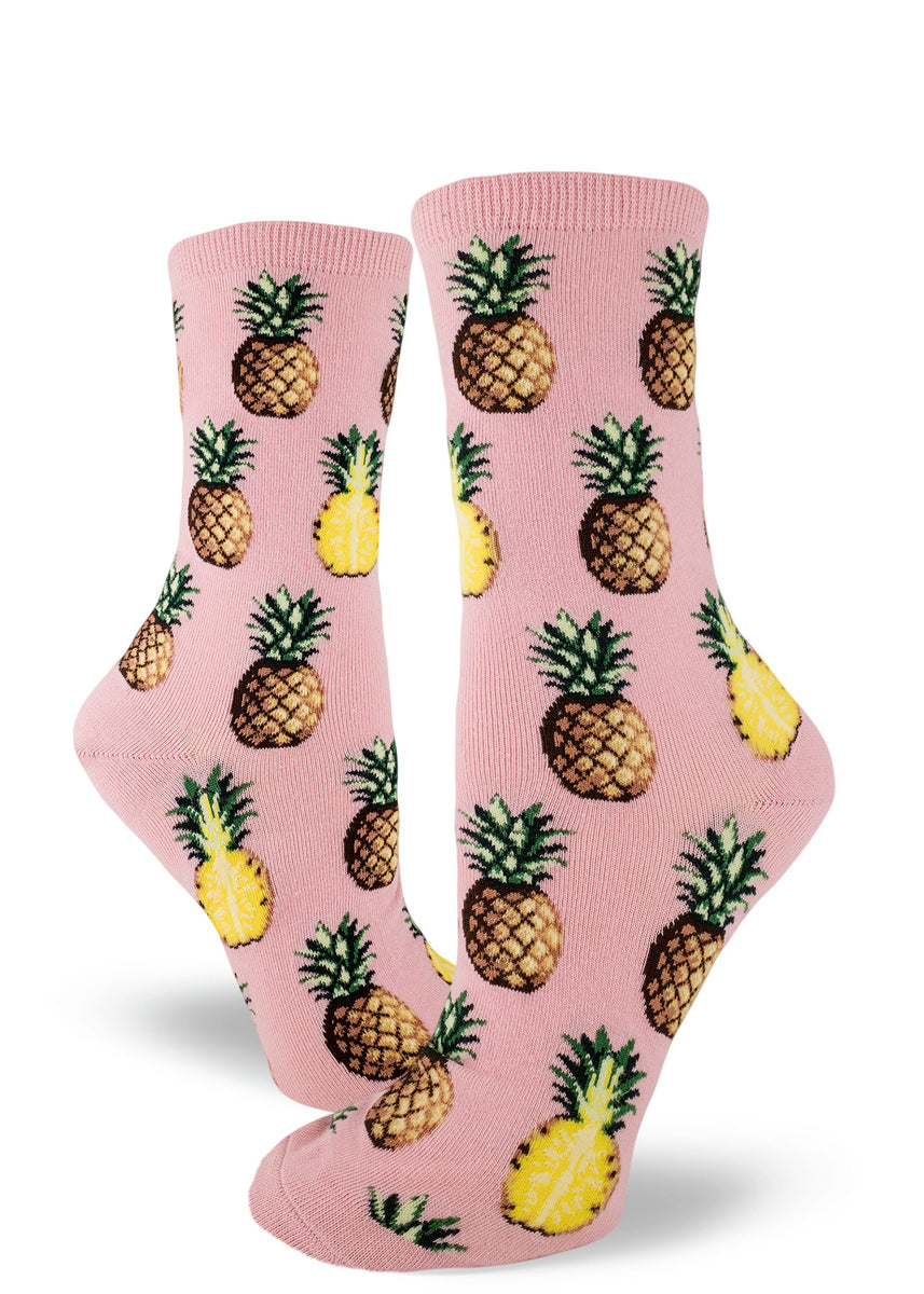 Tropical pineapple socks for women with pineapples sliced in half and whole pineapples on a light pink background
