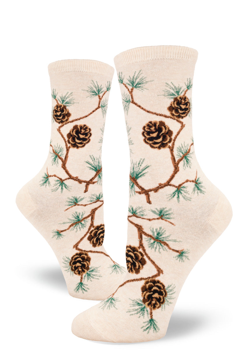 Crew socks for women feature pine branches with green needles and brown pinecones on a cream background.