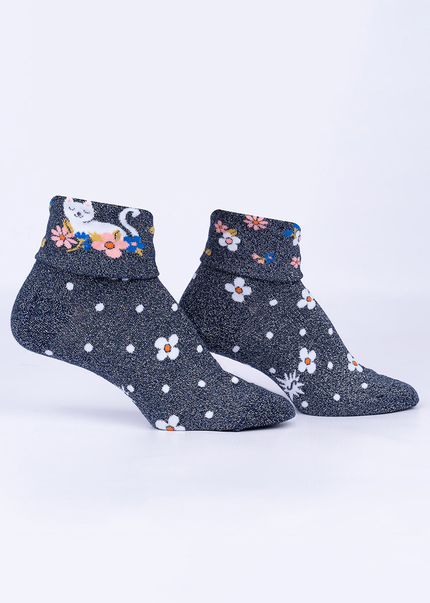 Shimmering metallic silver and black socks with daisies and polka dots feature a cuff that can be turned down to reveal a white cat napping in the blossoms.