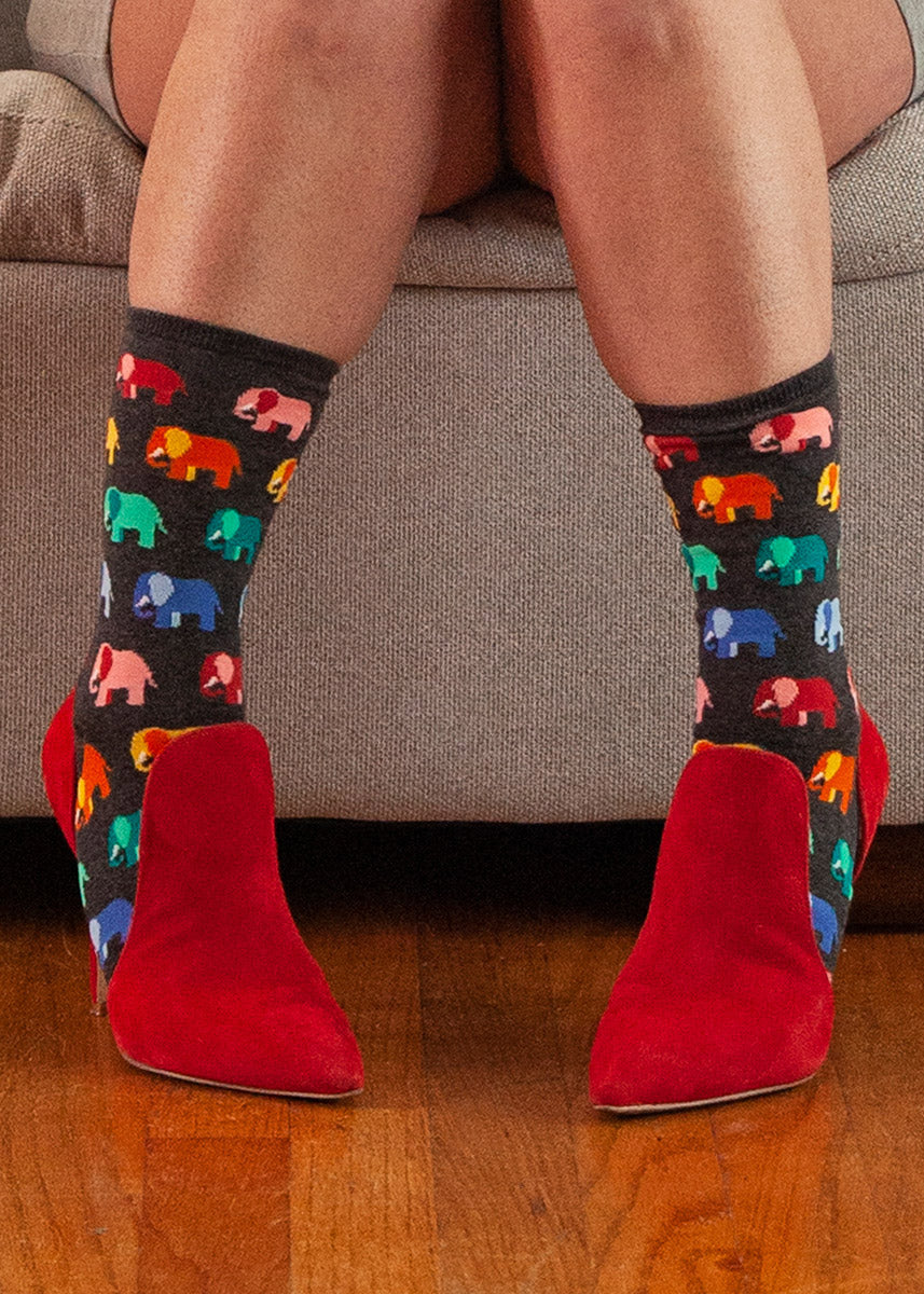 Women's crew socks feature a repeating pattern of elephants in rainbow colors over a heather charcoal background.