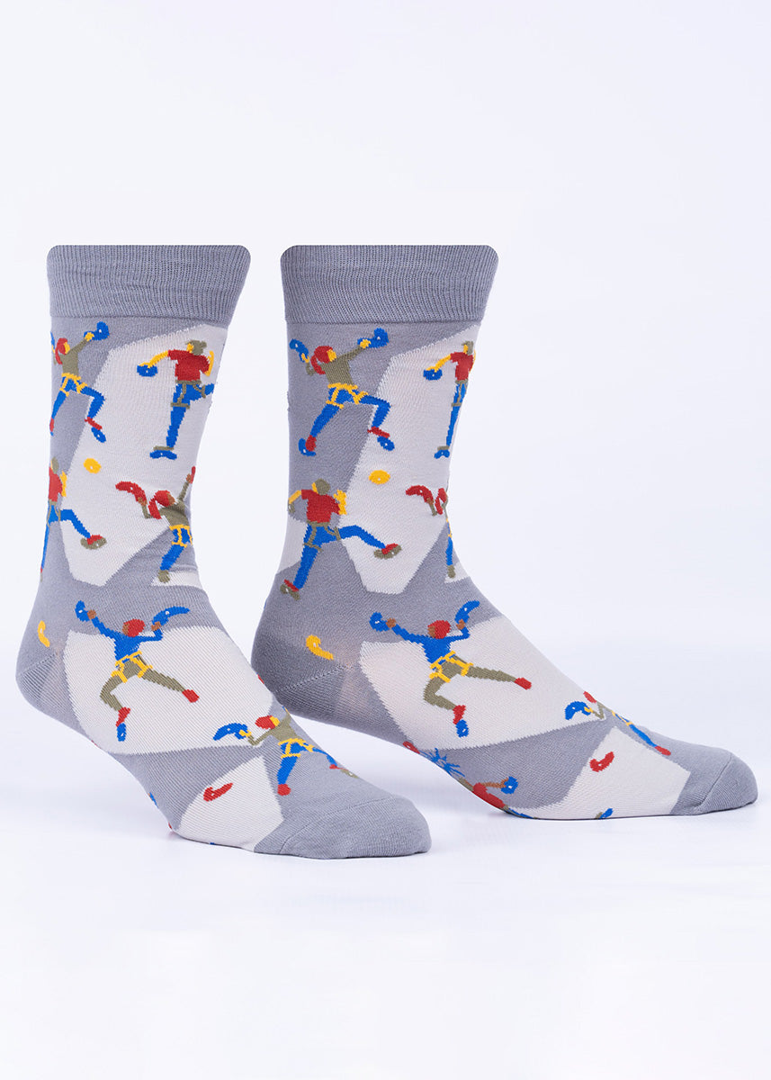 Novelty rock climbing socks for men show people on a climbing wall reaching for hand and footholds in bright red and blue socks.