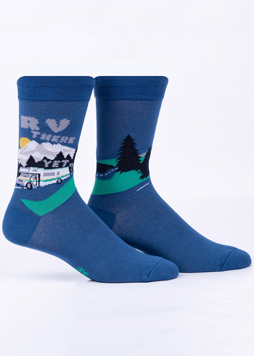 Blue men's crew socks with RVs driving down the open road with the words “RV There Yet?” written in clouds of exhaust, all with a background of trees and mountains.