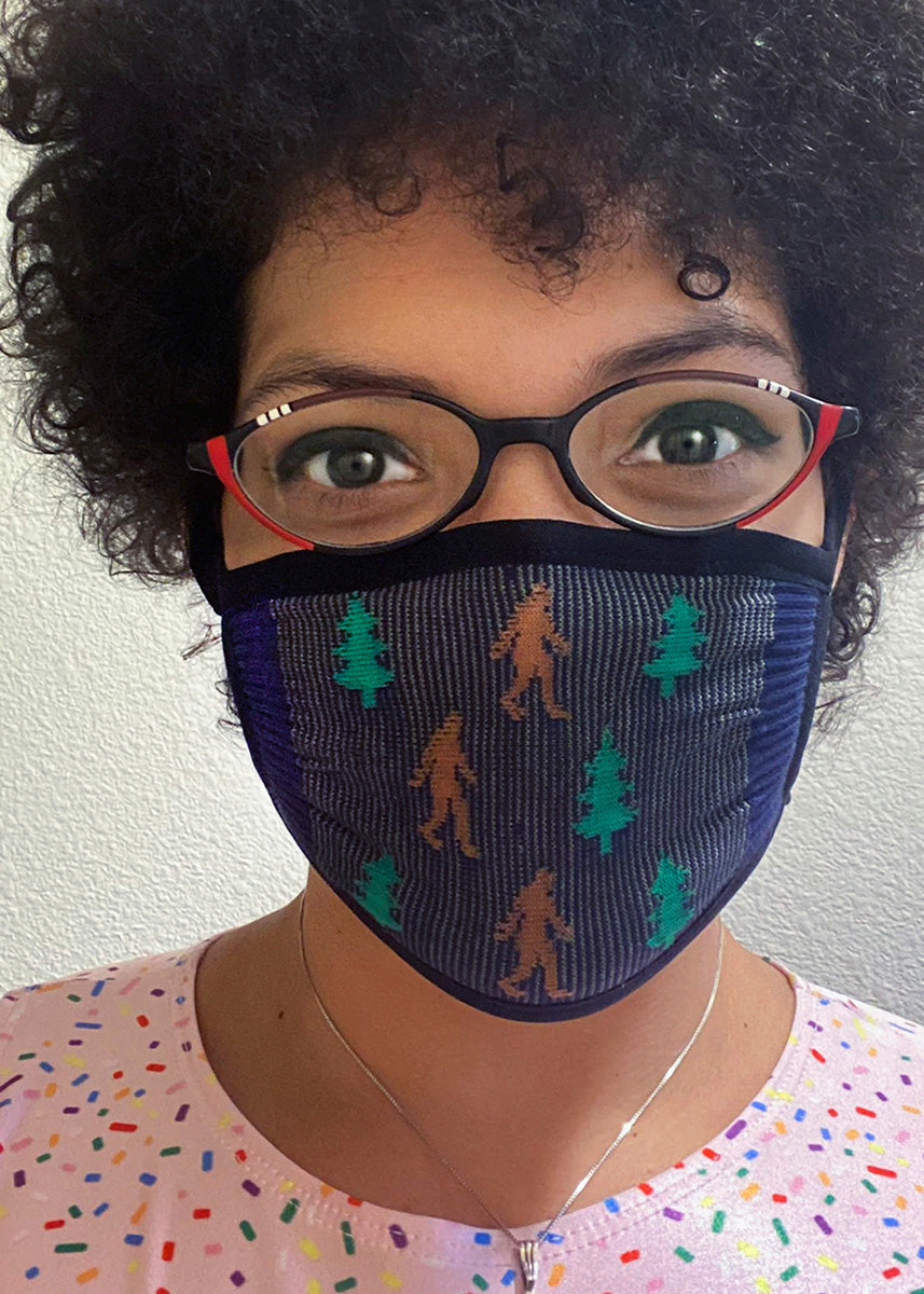 A navy face mask with a pattern of Sasquatches and pine trees.