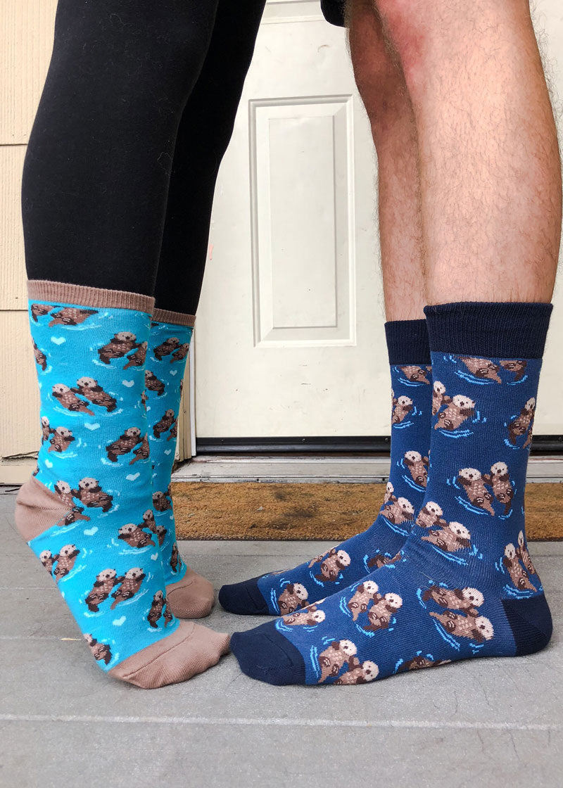 A female model wearing otter-themed novelty socks stands on her tip toes facing a male model who is wearing matching otter socks