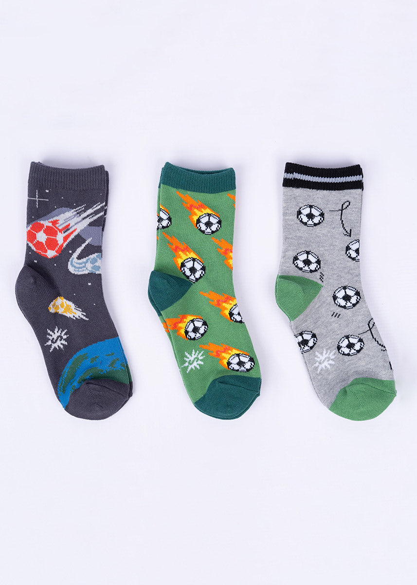 Three pairs of coordinating socks for kids: glow-in-the-dark soccer ball comets orbiting planet Earth, flaming soccer balls flying across a green field and black and white balls with arrows that look like a page out of a playbook.