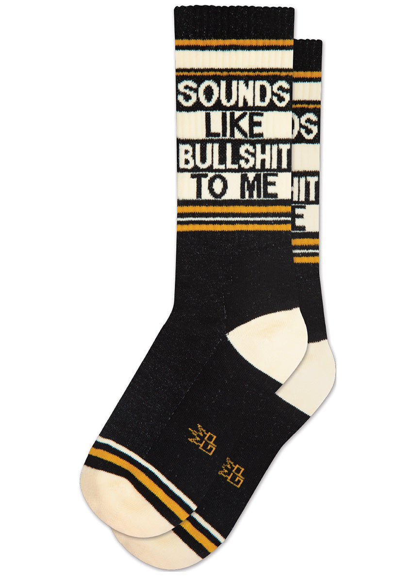 Retro athletic-style crew socks say “SOUNDS LIKE BULLSHIT TO ME” on a black background with stripes in ivory and gold.