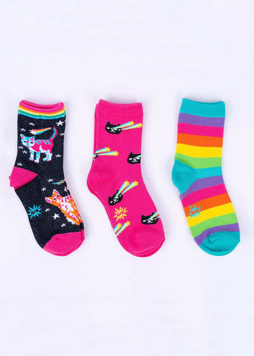 Three pairs of coordinating socks for kids including a metallic space cats design, a pair with black cats with shooting star eyes, and a bright rainbow-striped pair.