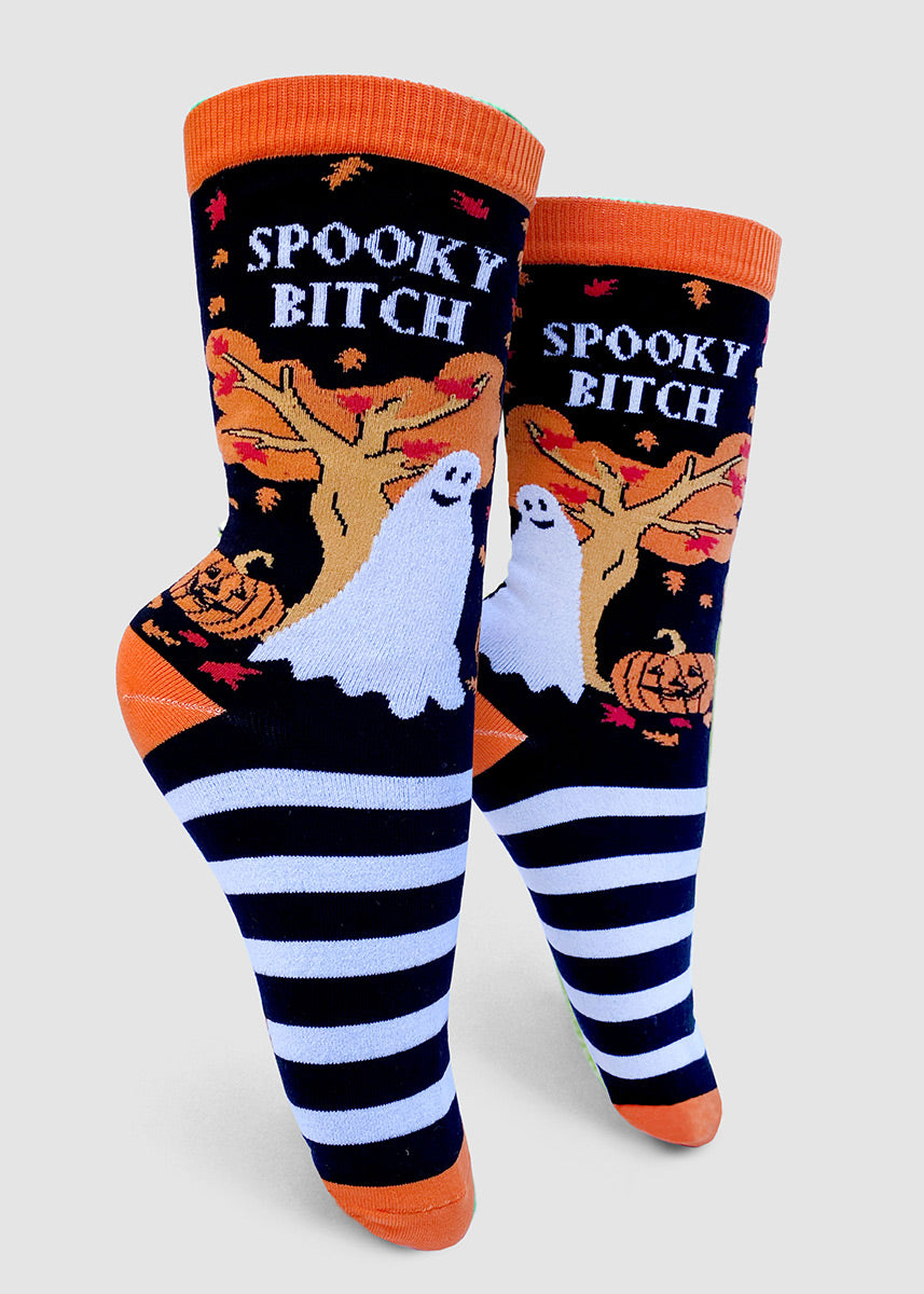 Funny Halloween socks for women feature a smiling ghost and a jack-o'-lantern under an autumn tree with the words, "Spooky Bitch."