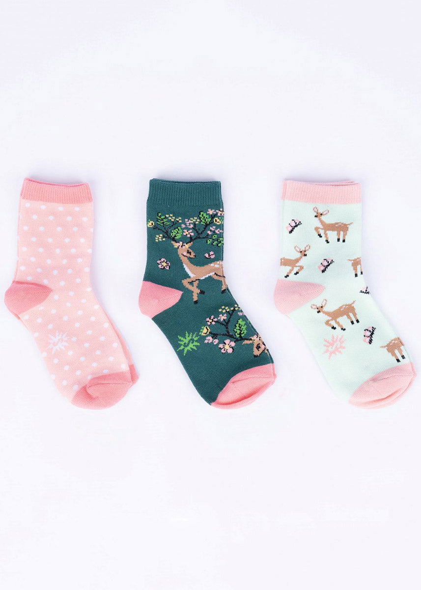 Three coordinating spring-themed sock designs for kids including a pair with fawns and pink butterflies, another with a buck with plants and flowers growing from its antlers, and a pair in pink with white polka dots.