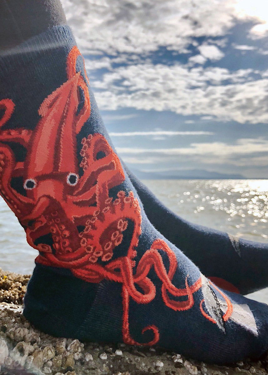 Crew socks for women show a giant orange squid pulling the tail of a whale on a heather navy background.