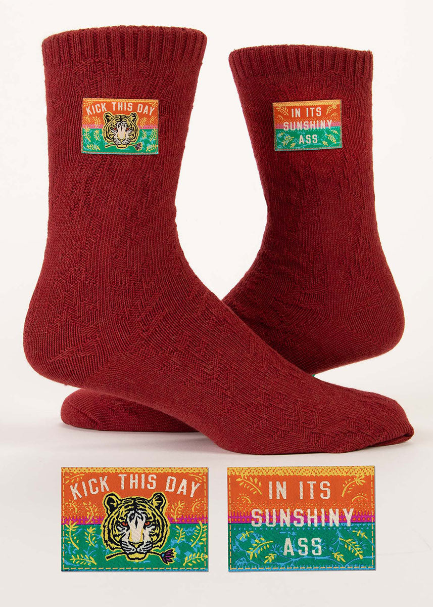 Vibrant rust red organic cotton socks knit with a textural foliage pattern and embellished with small decorative tags that say “KICK THIS DAY IN ITS SUNSHINY ASS&quot; along with a tiger face.