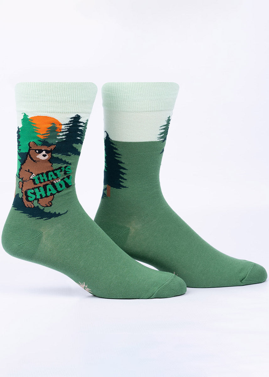 Green men's crew socks with a design featuring big brown grizzly bears walking upright while sporting black sunglasses as they turn their backs on the setting sun and hold up the words “That's Shady.”