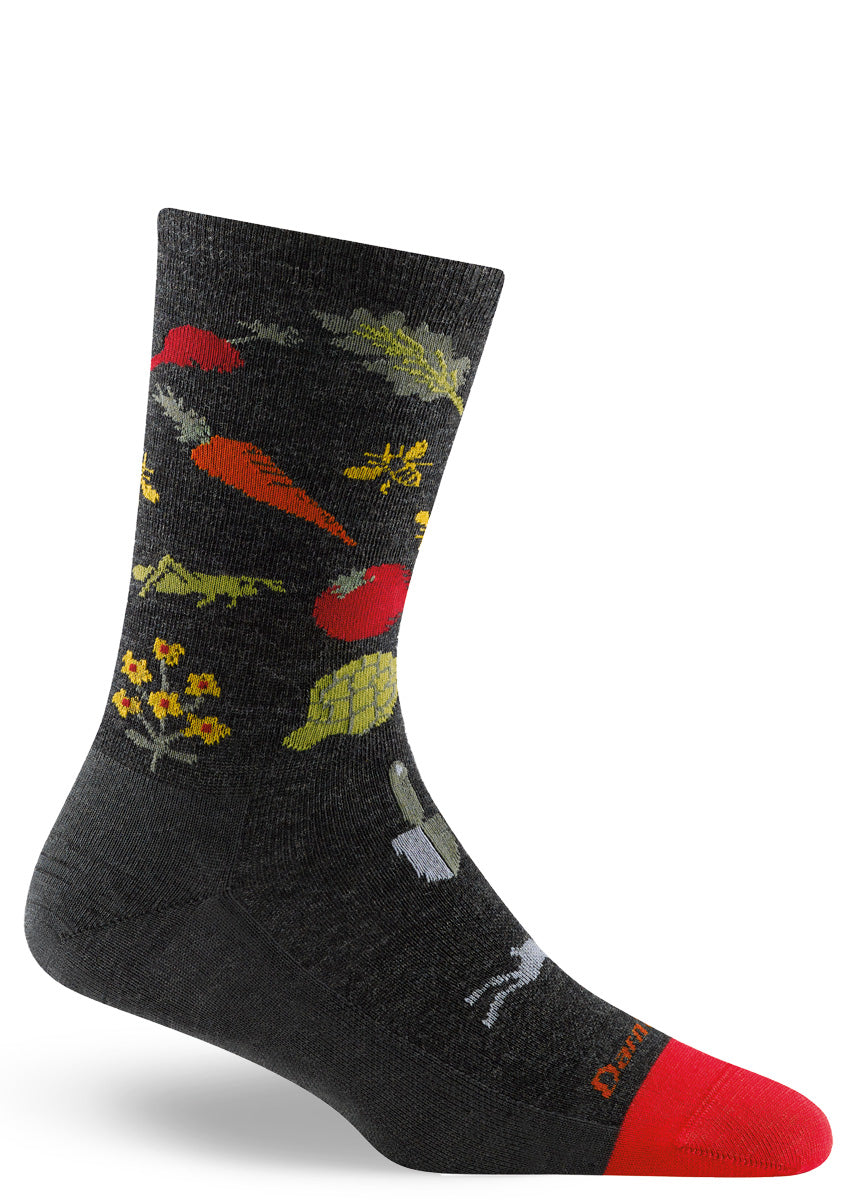 Wool socks for women feature a garden design of veggies, flowers, bees, and tools on a dark gray background.