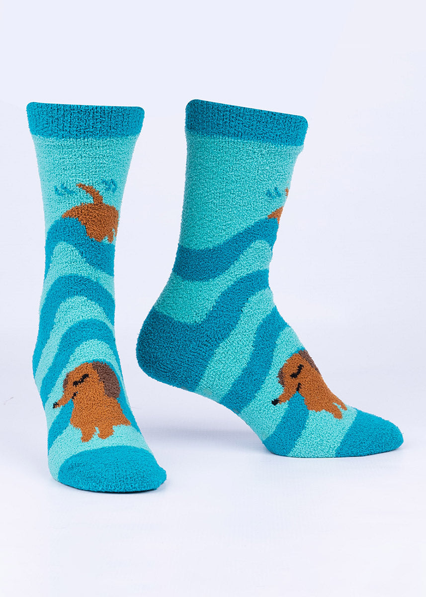 A cute Dachshund dog burrows under striped blankets on these crew-high fuzzy slipper socks with a teal background.